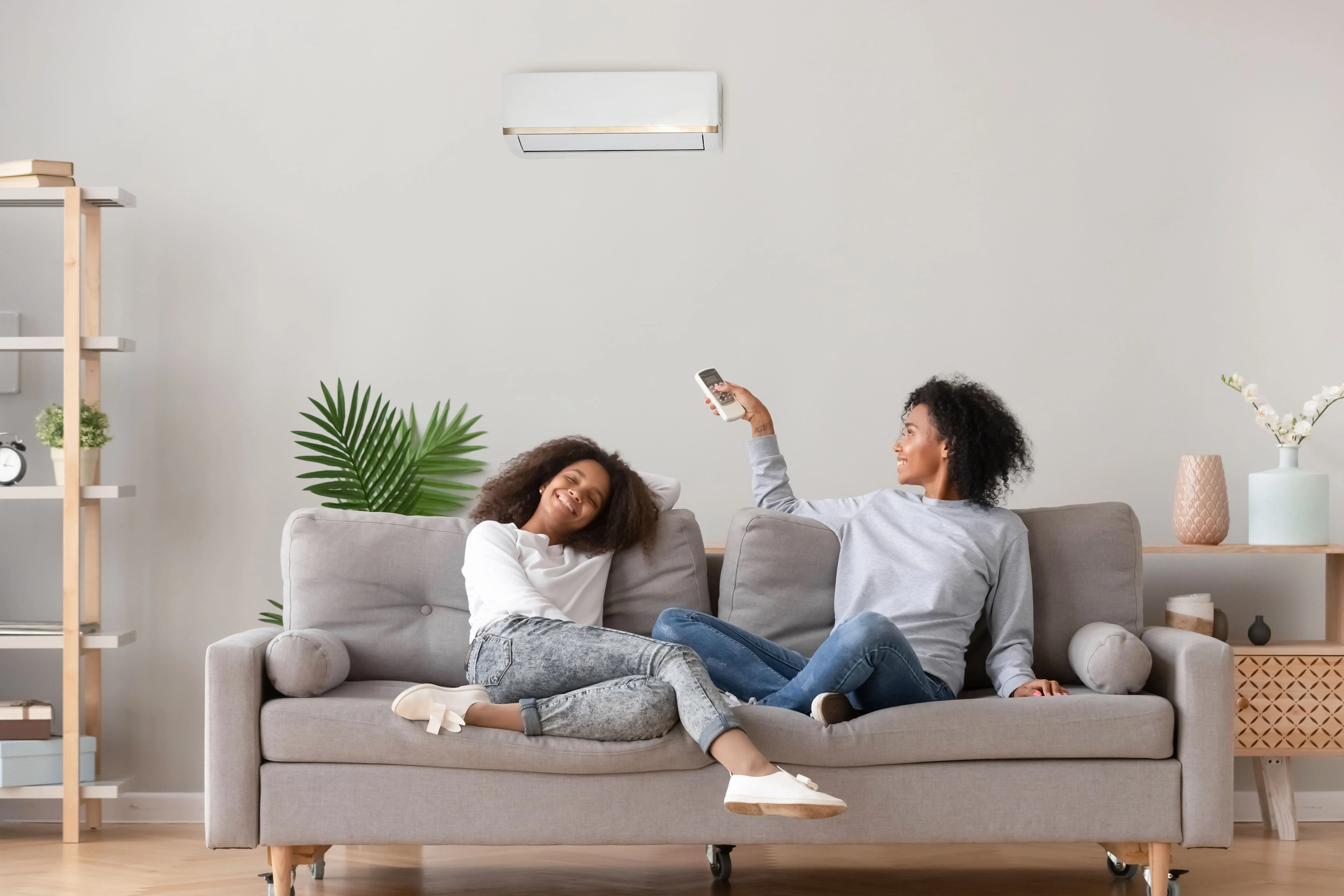 2 women sitting comfortably on a couch setting the thermostat with a remote control